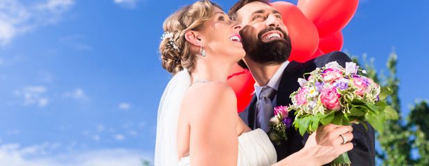 Bride and groom at wedding with read helium balloons