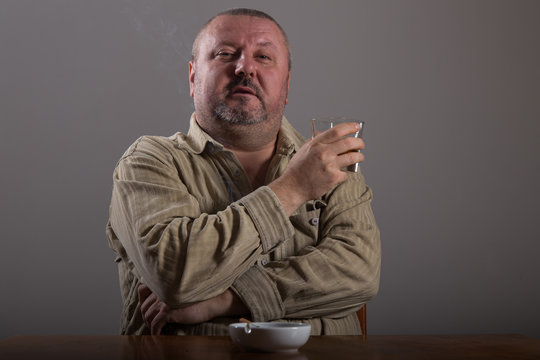 Alcoholism: portrait of a lonely, desperate man drinking alcohol and smoking cigarette