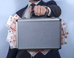 Man in suit holds metal briefcase full of money