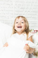 Little blonde girl playing in bed