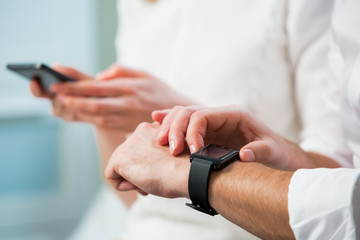 Close up of man and woman hands working on line and synchronising a modern smart watch with smart phone in office