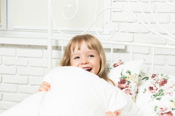 Little blonde girl playing in bed