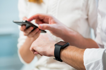 Close up of man and woman hands working on line and synchronising a modern smart watch with smart phone in office