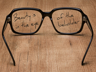 Glasses, resting on a table, and a text written on the glass.Beauty is in the eye of the beholder