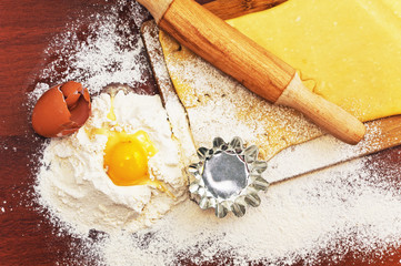 Set for home baking on a brown background with flour. Rolling pin, dough, baking form, eggshell. 