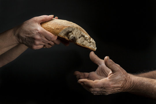 Mano di donna dona pagnotta di pane a un povero senzatetto. Concetto di povertà , emarginazione , fame nel mondo 
