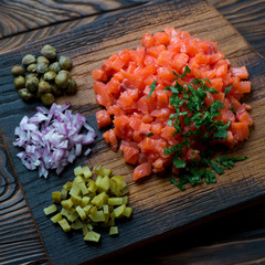 Closeup of salmon tartar with pickles, capers, onion and parsley