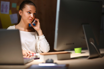 Young woman working in office, sitting at desk and talk on the phone