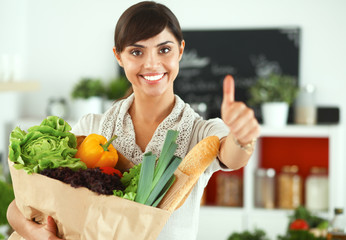 Young woman holding grocery shopping bag with vegetables Standing in the kitchen and showing ok