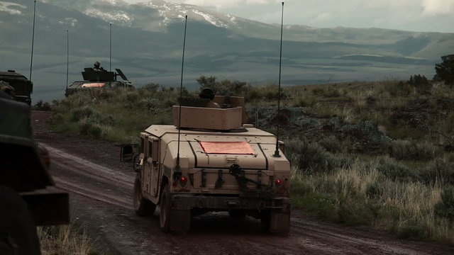 Humvees convoy traveling on a dirt road, training explosives create smoke and explode.