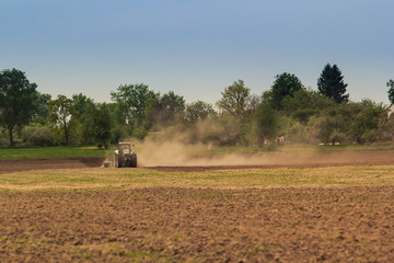 cultivator operates on ploughed field raises dust in spring