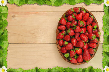 Strawberries in basket on wooden table with a frame of strawberry leaves