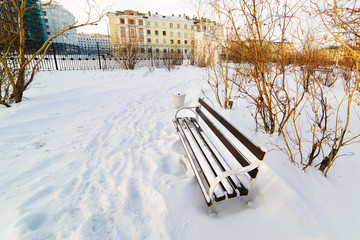 An empty bench in the snow-covered city park