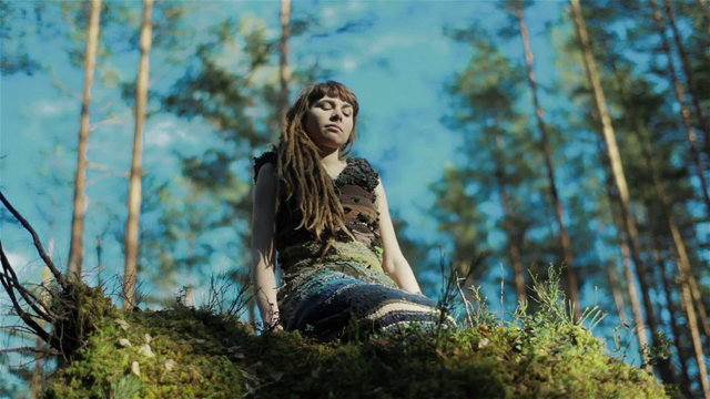 Young woman in the forest sitting on mossy hill and touching plants around her. Close up