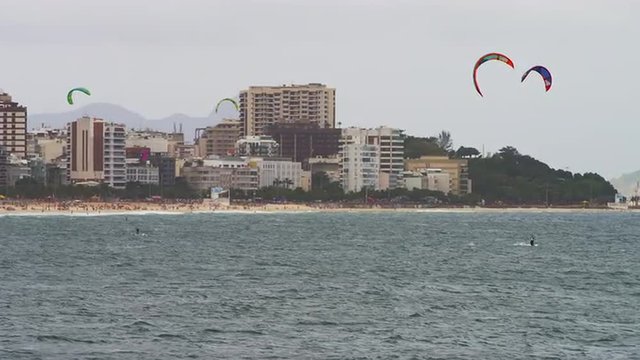 Pan shot of three parasailing surfers with Copacabana city.