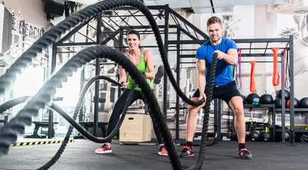 Foto op Plexiglas Frau und Mann im Fitnessstudio mit battle rope © Kzenon