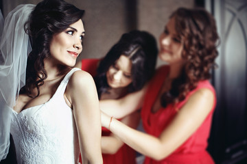 Naklejka premium Bridesmaids in red dresses help beautiful bride prepare for her