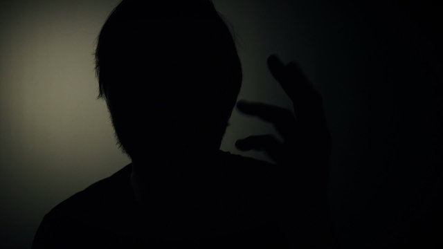 Person in witness protection program during police interview, silhouette of male giving statement to the police detectives during crime interrogation in dark room.