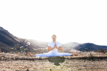 Asian man meditates in yoga position on high mountains above blue sky. 