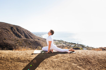 Fototapeta na wymiar Asian man meditates in yoga position on high mountains above blue sky. 