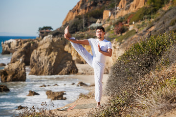Asian man meditates in yoga position on high mountains above blue sky. 