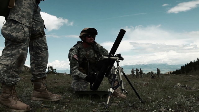 Slow panning shot of soldiers firing a mortar.