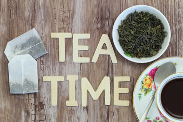 Tea time written with wooden letters, tea bags and dried tea leaves
