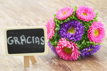 Gracias (thank you in Spanish) written on mini blackboard with colorful aster bouquet
