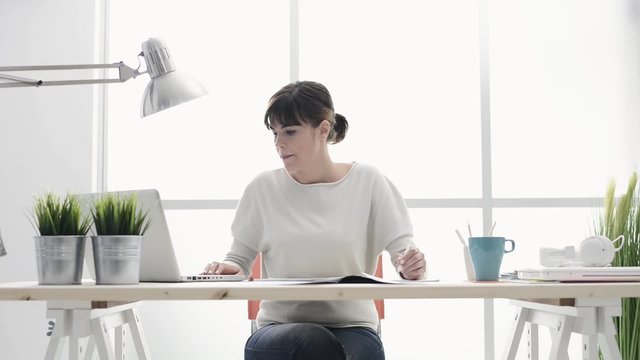 Young female freelance working at home, using a laptop and sketching on paper, business and creativity concept