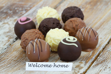 Welcome home card with assorted chocolates on rustic wooden surface
