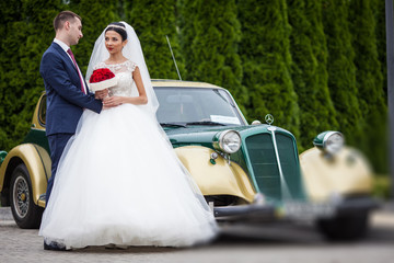 Happy bride and groom hugging and posing near old retro car befo