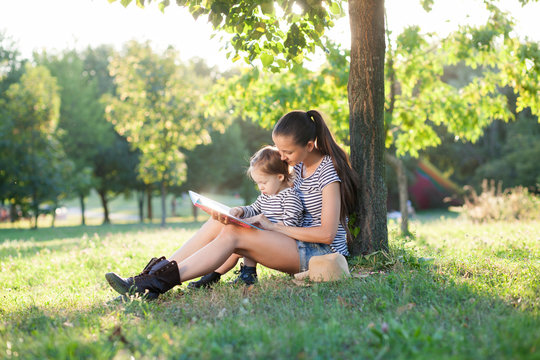 Mother and toddler sitting under the tree during summer leisure