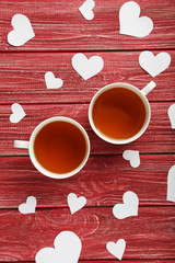 Fototapeta na wymiar Love hearts with cups of tea on a red wooden table