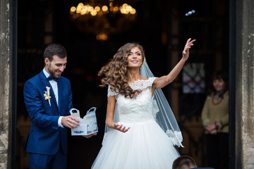 Happy newlywed husband and wife coming out of church and throwing candy to everyone