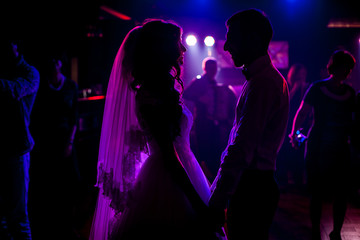Romantic couple of newlyweds silhouettes posing at wedding reception surrounded by purple lights