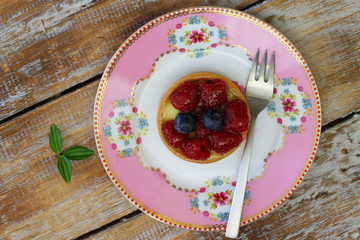 Crunchy and creamy tartelette with raspberries and blueberries on pink plate rustic wooden surface
