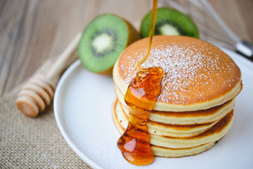 pouring syrup on stack of pancake on white plate and sackcloth w