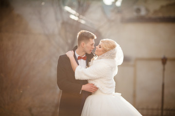Fototapeta premium Happy newlywed groom hugging blonde beautiful bride at sunset in