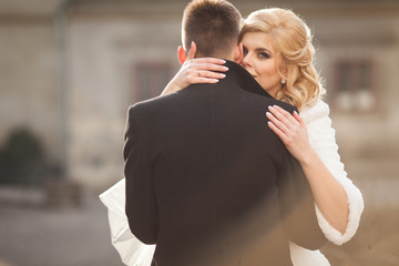 Beautiful blonde bride kissing handsome groom in black coat in t