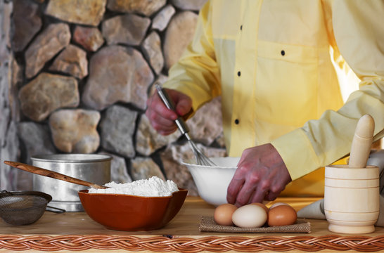 flour, eggs, a sieve and a mortar, and a male cook in a yellow garment whisk the whisk the batter. Concept of rustic kitchen, selective focus. Copy space. Free space for text