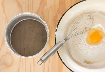 broken egg in flour, whisk and aluminum sieve for sifting on a wooden table. top view closeup
