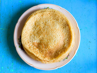Pancake made from wheat flour in an old ceramic bowl on a blue background. Rustic style. Top view closeup. Traditional Russian dish on Shrove Tuesday