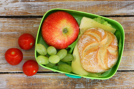 School lunch box with cheese sandwich, red apple, grapes and cherry tomatoes
