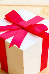 Gift box with red bow on wooden background.