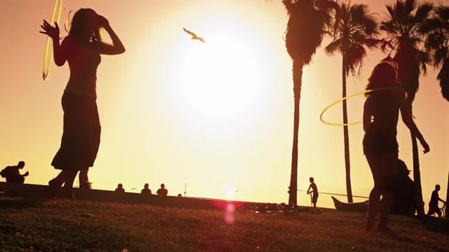 Slow motion lens flare shot of hula hoop performance by two women near Venice Beach, California