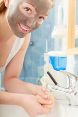 woman removing facial clay mud mask in bathroom