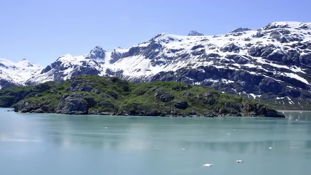 Traveling view of snow covered mountains and small ice glaciers floating in Glacier Bay