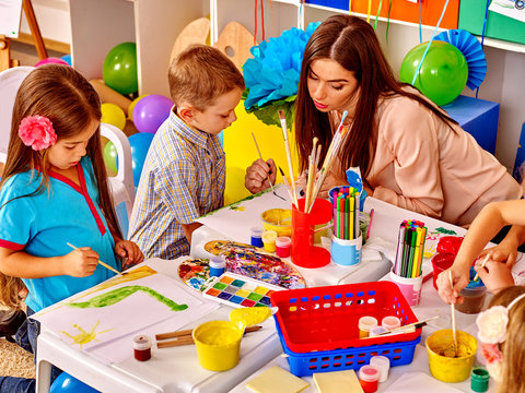 Two children with female teacher painting  in  kindergarten . 