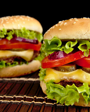 Big cheeseburgers on wooden mat on black background