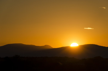 A colorful sunset in Santa Fe, New Mexico with a sun hiding behind mountains.